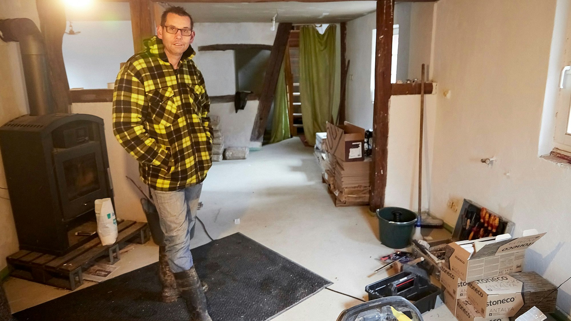 Ein Mann steht in einem Zimmer eines Fachwerkhauses. Dort wird saniert, Baumaterialien und Werkzeug liegen an der Wand.