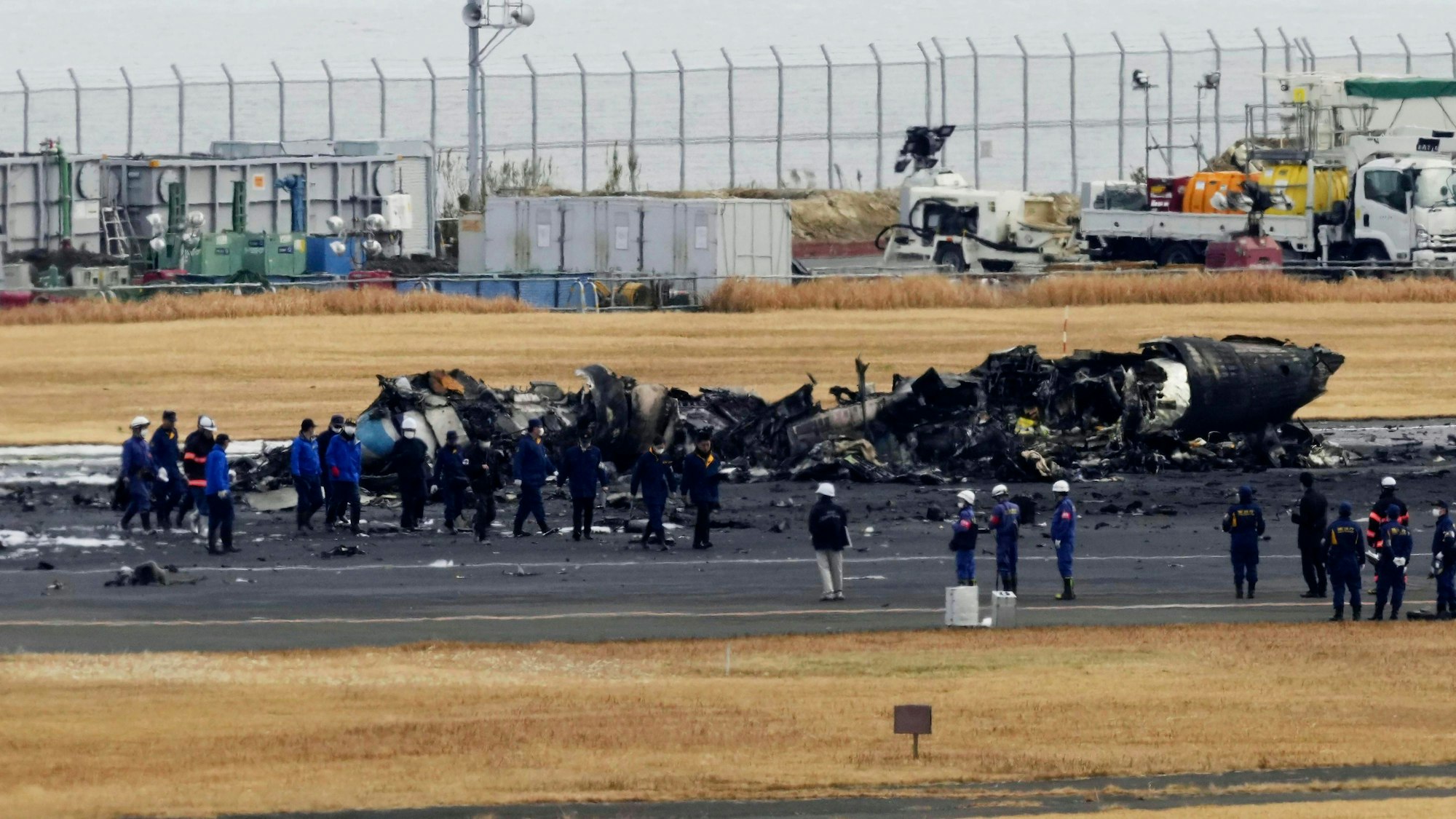 Feuerwehrleute versammeln sich um das ausgebrannte Flugzeug der japanischen Küstenwache auf dem Flughafen Haneda am Mittwoch, 3. Januar 2024, in Tokio, Japan.