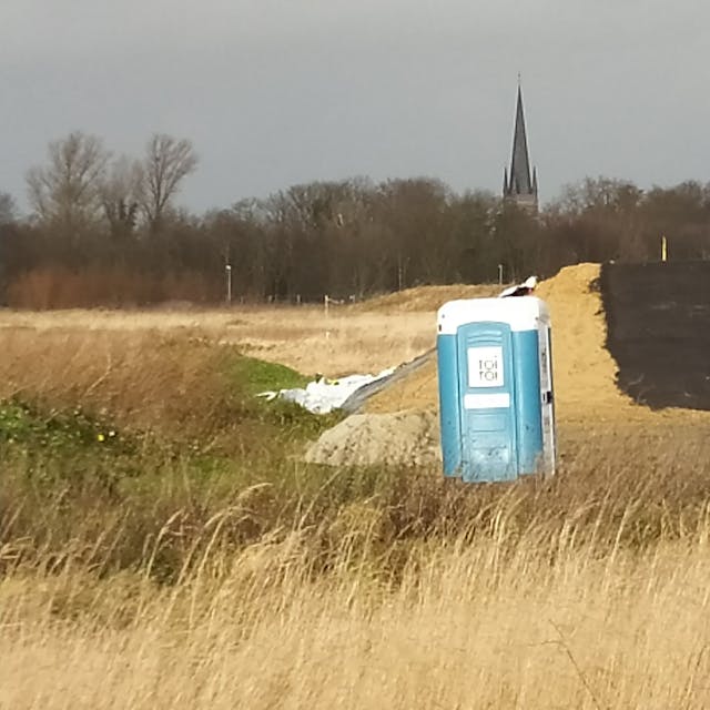 Eine künstlicher Hügel, ein Toilettenhäuschen und ein kleiner weißer Baucontainer markieren die Stelle, an der gebaut worden ist.