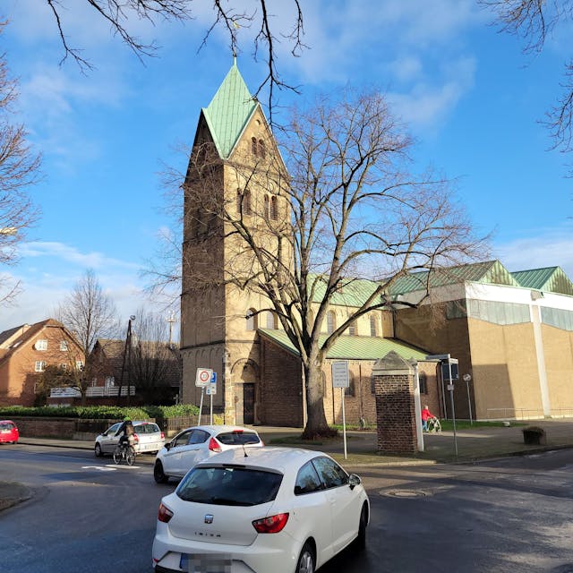 Auf einer Kreuzung&nbsp; biegen zwei Fahrzeuge nach links ab, im Hintergrund ist eine Kirche zu sehen.