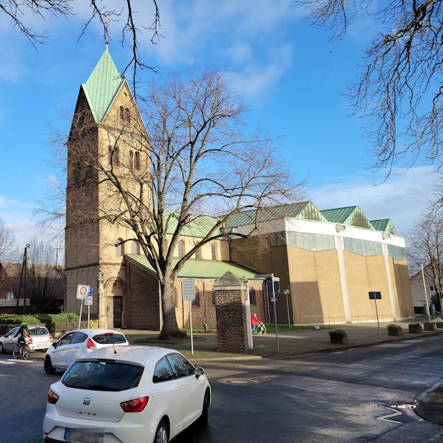 Auf einer Kreuzung&nbsp; biegen zwei Fahrzeuge nach links ab, im Hintergrund ist eine Kirche zu sehen.