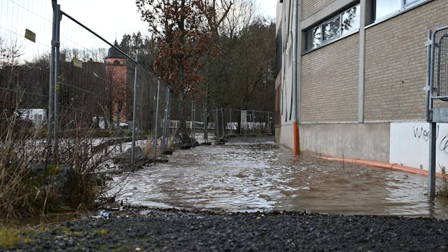 Links hinter einem Bauzaun ist die Olef in Schleiden. Der Fluss führt Hochwasser, das Wasser reicht bis ans Sturmius-Gymnasium heran.
