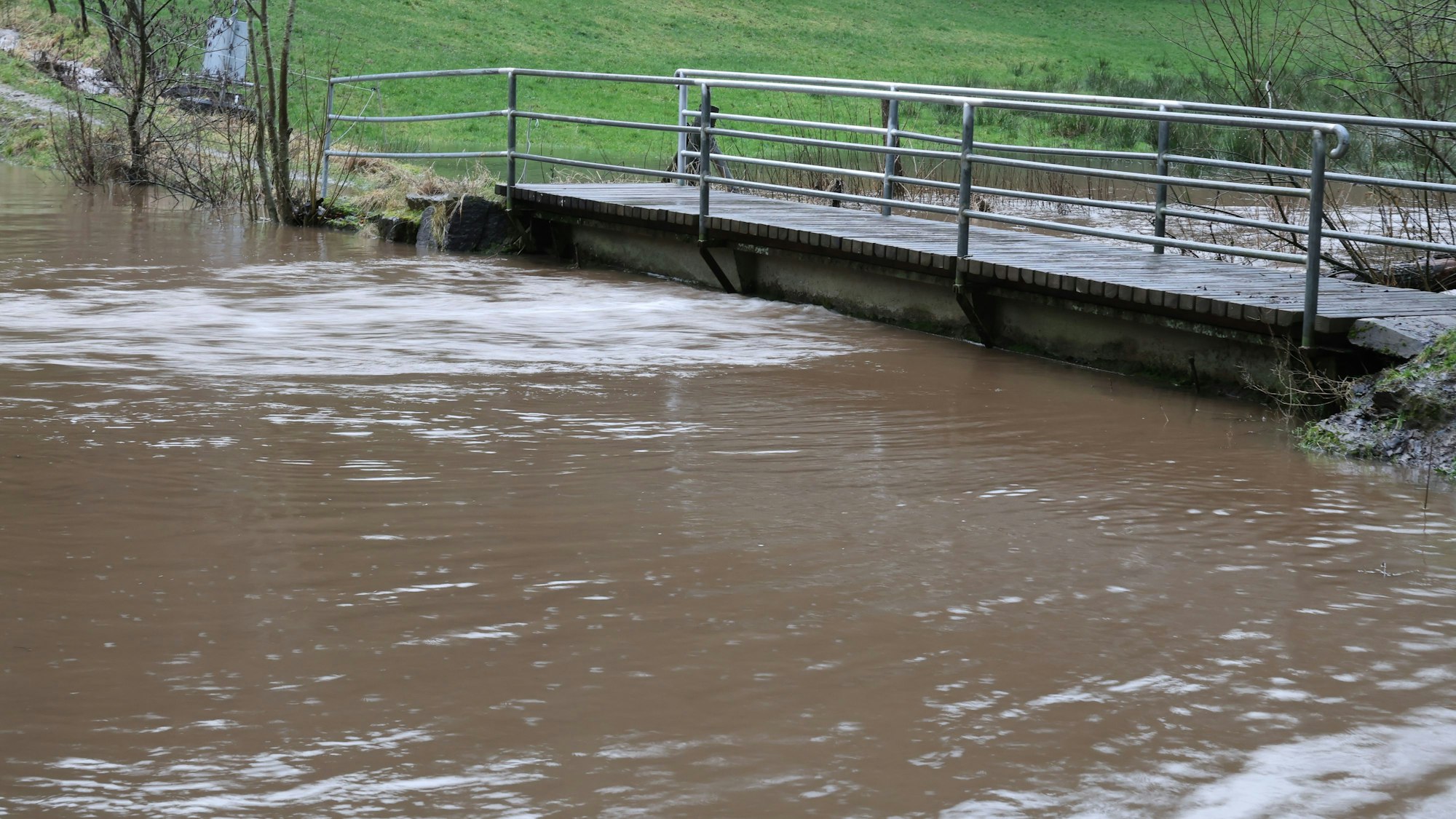 Der Wolferter Bach führt Hochwasser. Das Wasser reicht bis zur Unterkante einer Brücke.