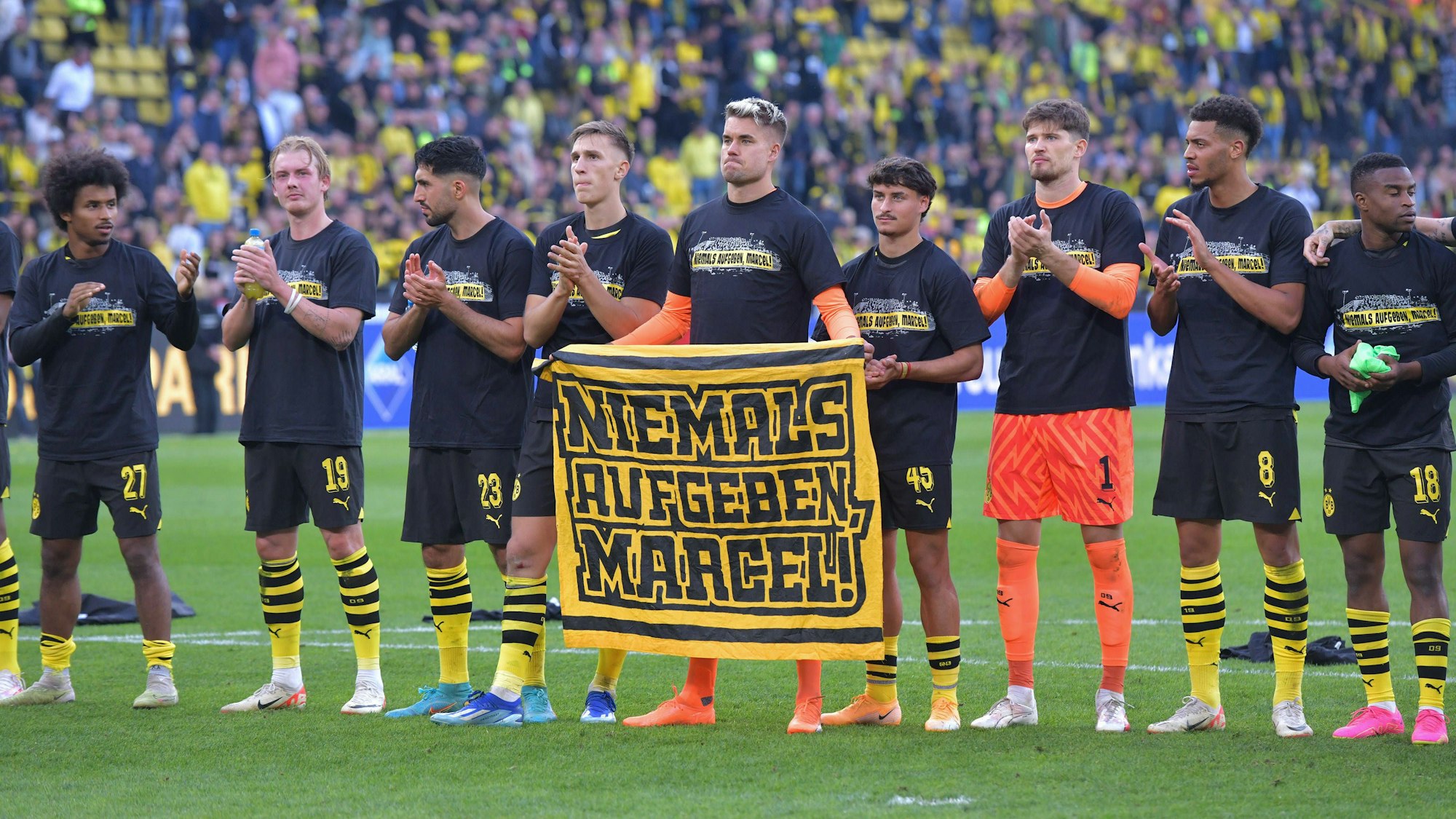 Die Profis von Borussia Dortmund halten ein Plakat mit der Aufschrift „Niemals aufgeben, Marcel“ hoch.