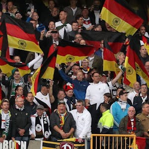 Fußball-Fans aus Deutschland stehen auf einer Tribüne und schwenken Flaggen.