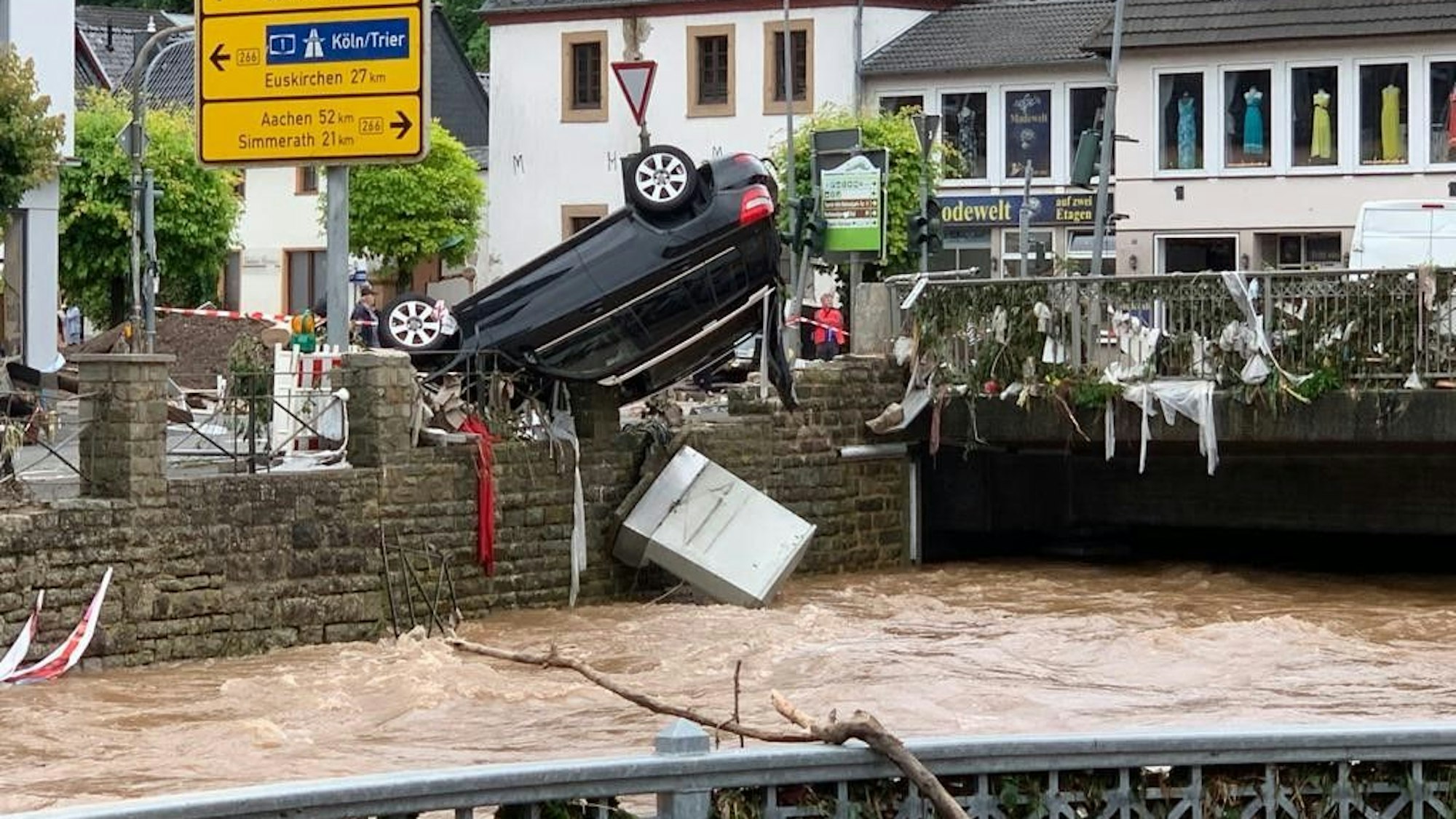 Am Morgen des 15. Juli 2021 zeigt sich das Ausmaß der Flutkatastrophe. In Gemünd hängt ein schwarzer SUV kopfüber auf dem Geländer an der Olef.