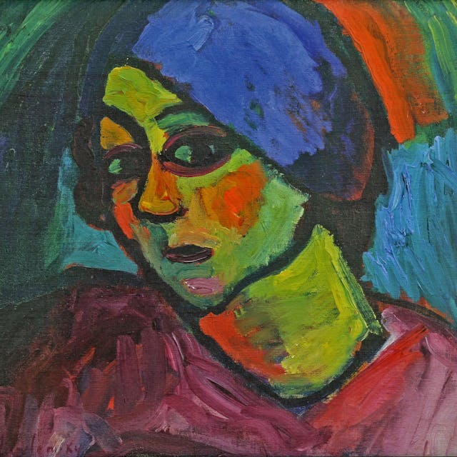 Eine Frau mit grüner Haut, roten Wangen und blauem Turban schaut den Betrachter an.