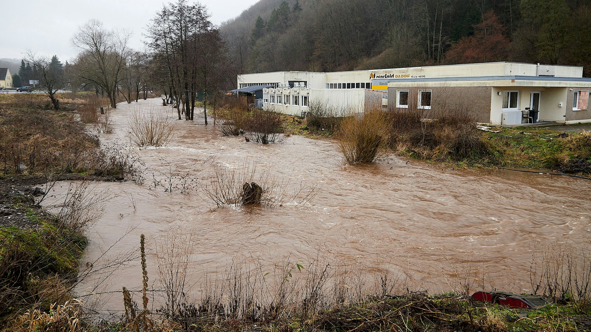 Das Bild zeigt die Hochwasser führende Olef, rechts die Pappenfabrik.
