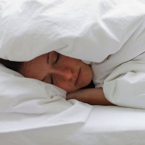 Kranke Frau liegt im Bett und zieht sich die Decke über den Kopf