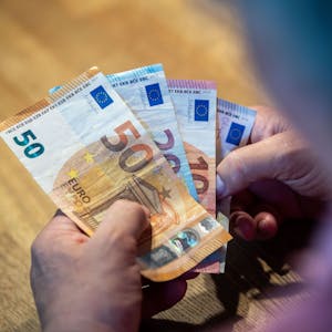 Ein älterer Mann sitzt an einem Tisch und einen 50-Euro-Schein, einen 20- und zwei 10-Euro-Scheine in der Hand.