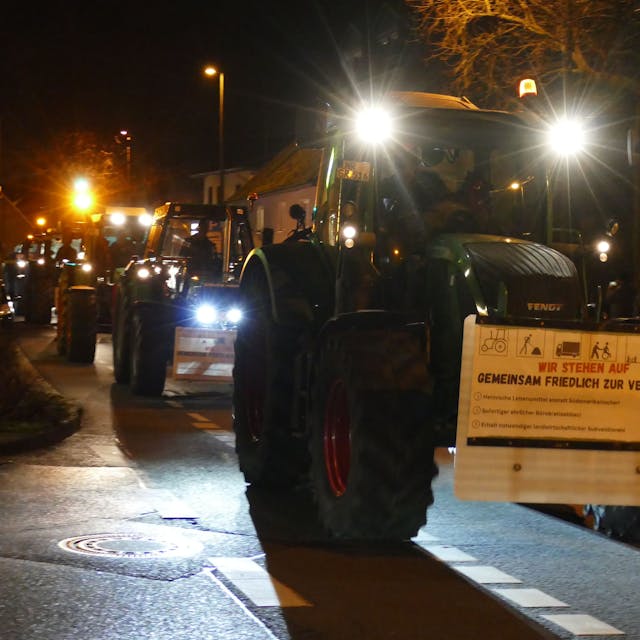 Ein Protestzug aus Traktoren fährt über eine Straße.