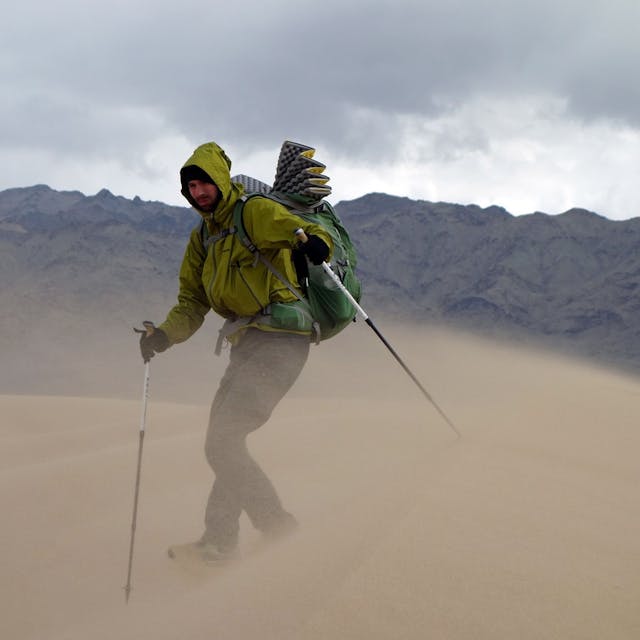 Das Bild zeigt Michael Giefer aus Lindweiler in der Wüste Gobi. Er hat einen Rucksack auf dem Rücken und geht mit Walking-Stöcken durch den vom Wind aufgewirbelten Sand einer Düne.