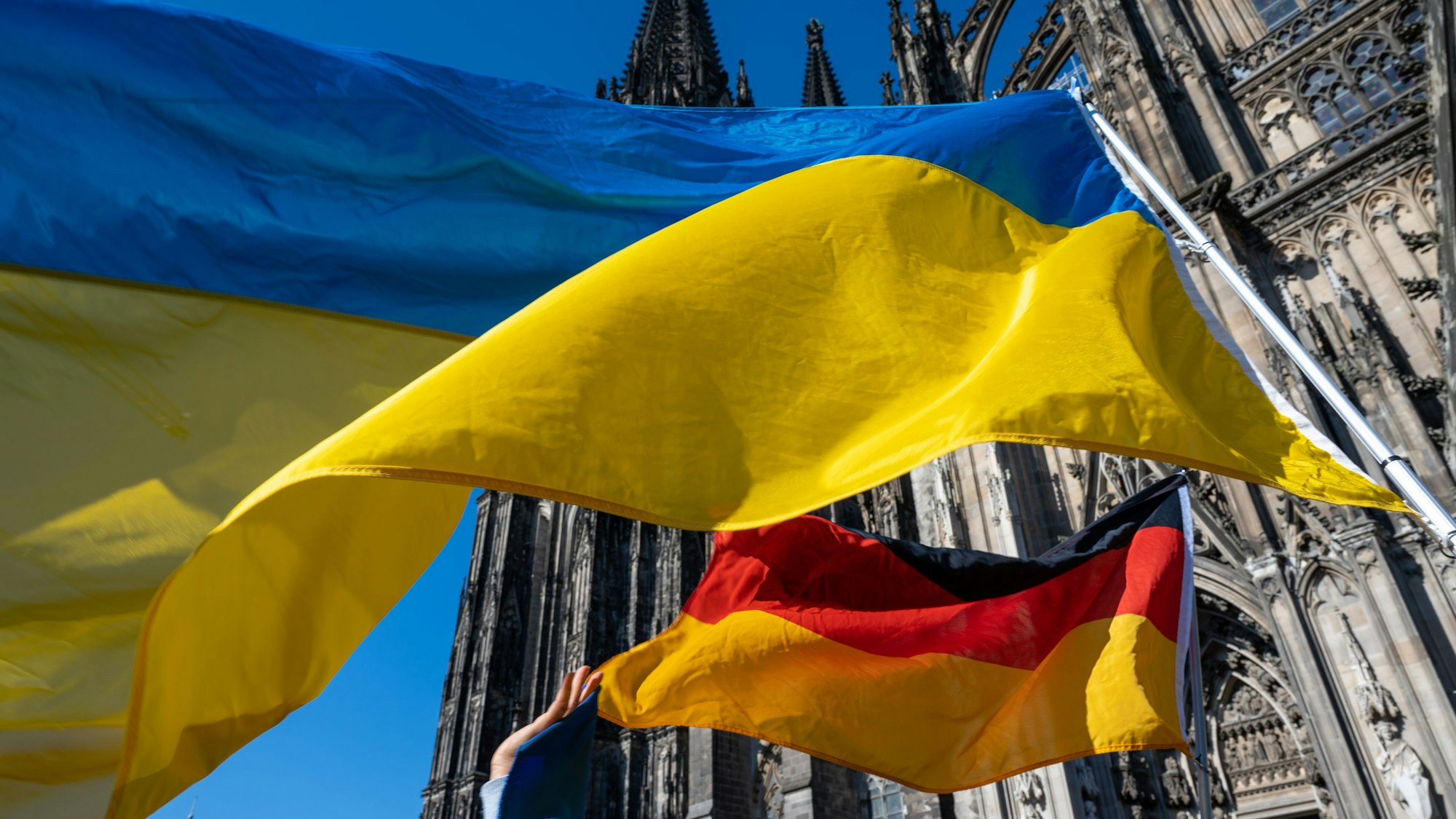 Eine ukrainische und eine deutsche Flagge wehen vor dem Kölner Dom.