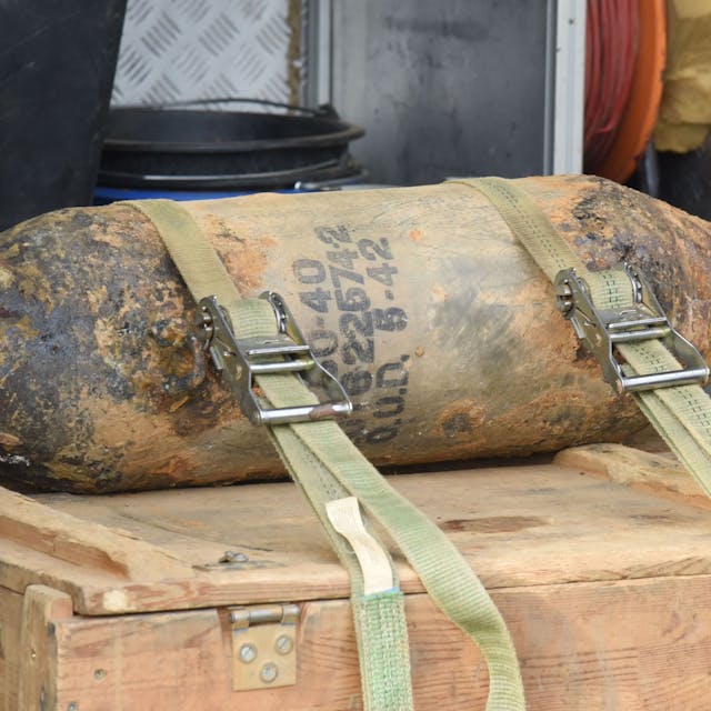 Eine entschärfte Fliegerbombe liegt auf einer Holzkiste und ist mit Gurten gegen Verrutschen gesichert.