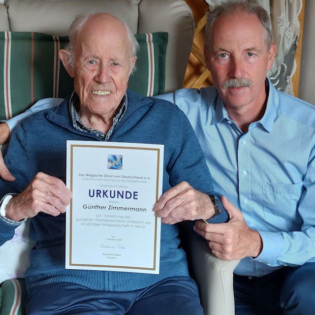 Zwei Männer sitzen nebeneinander, der linke Mann ist 96 Jahre alt und hält eine Urkunde in den Händen.