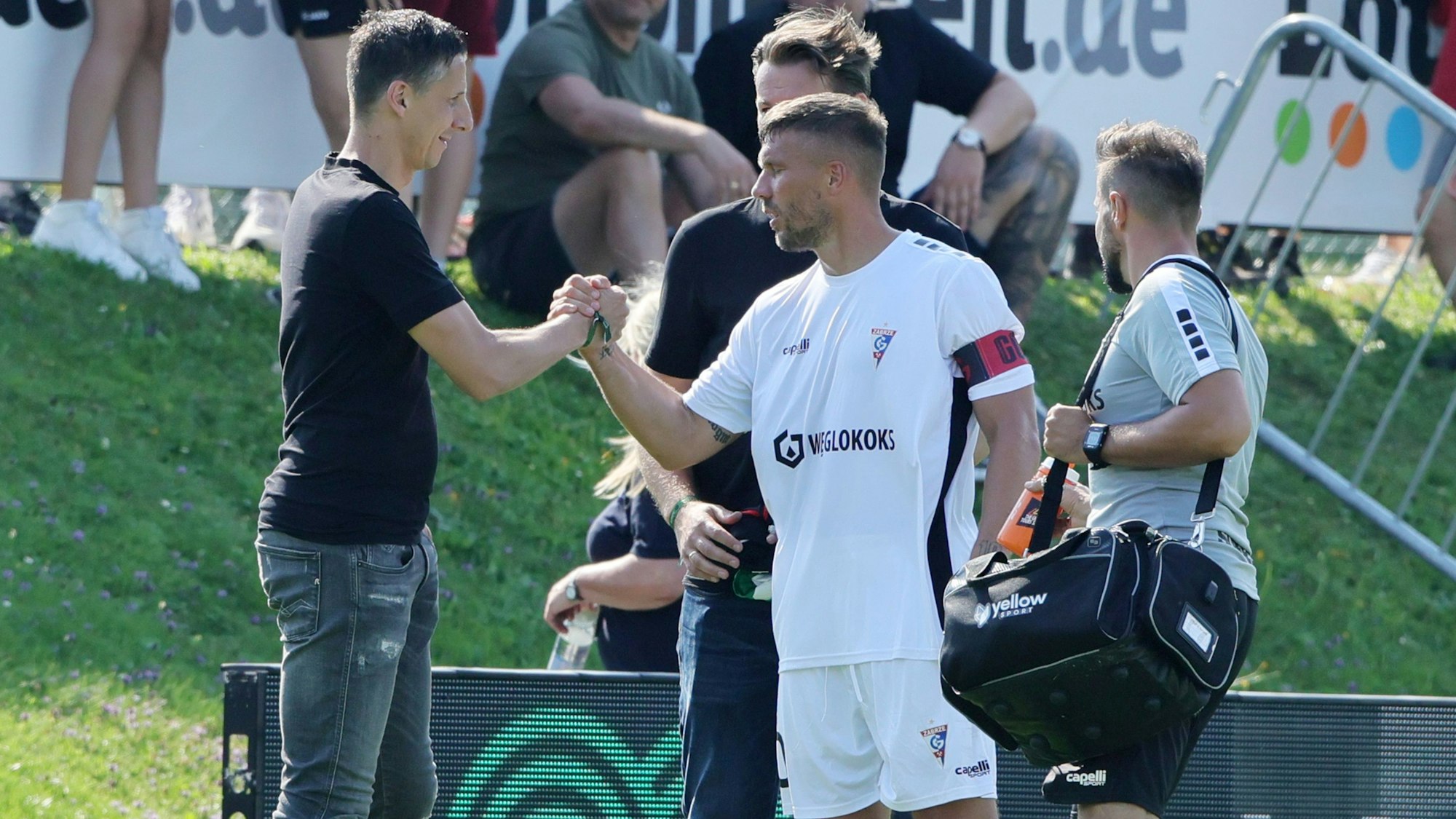Lukas Podolski und Christian Keller geben sich am Rande eines Testspiels die Hand.








