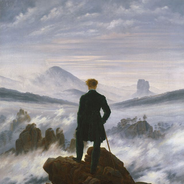 Ein Mann steht auf einem Gipfel und schaut auf eine neblige Landschaft.