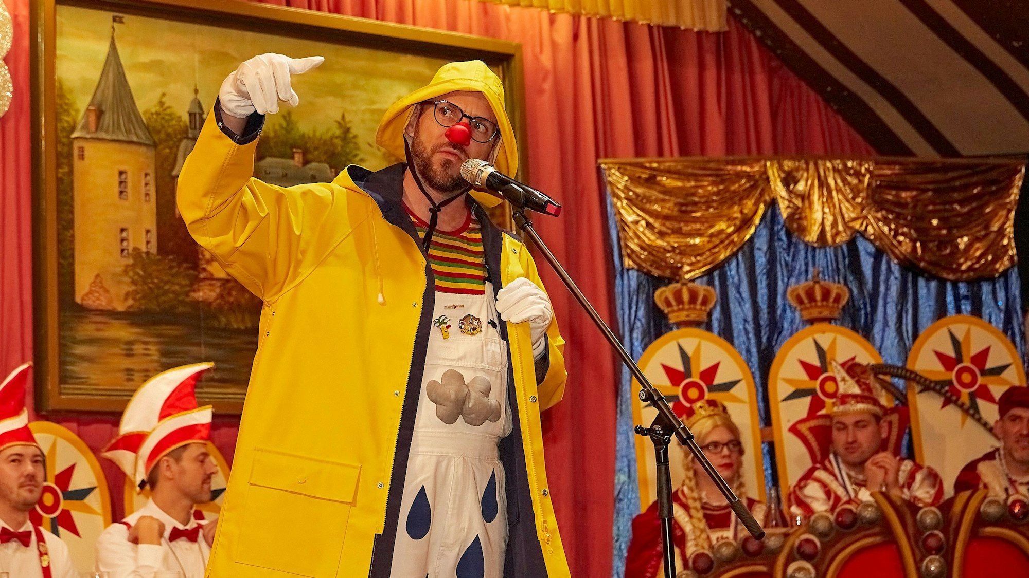 Das Bild zeigt Büttenredner Björn Wassong auf der Bühne – inklusive Regenjacke.