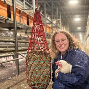 Jasmin Schleder im Stall, sie hält eine weiße Henne im Arm und lächelt in die Kamera.&nbsp;