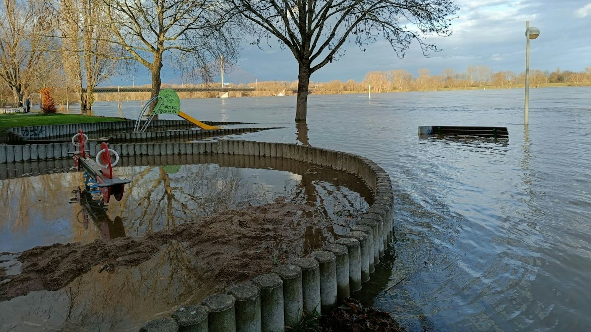 Wasser überflutet das Rheinufer in Bonn an der Nordbrücke und auch Teile eines Spielplatzes.
