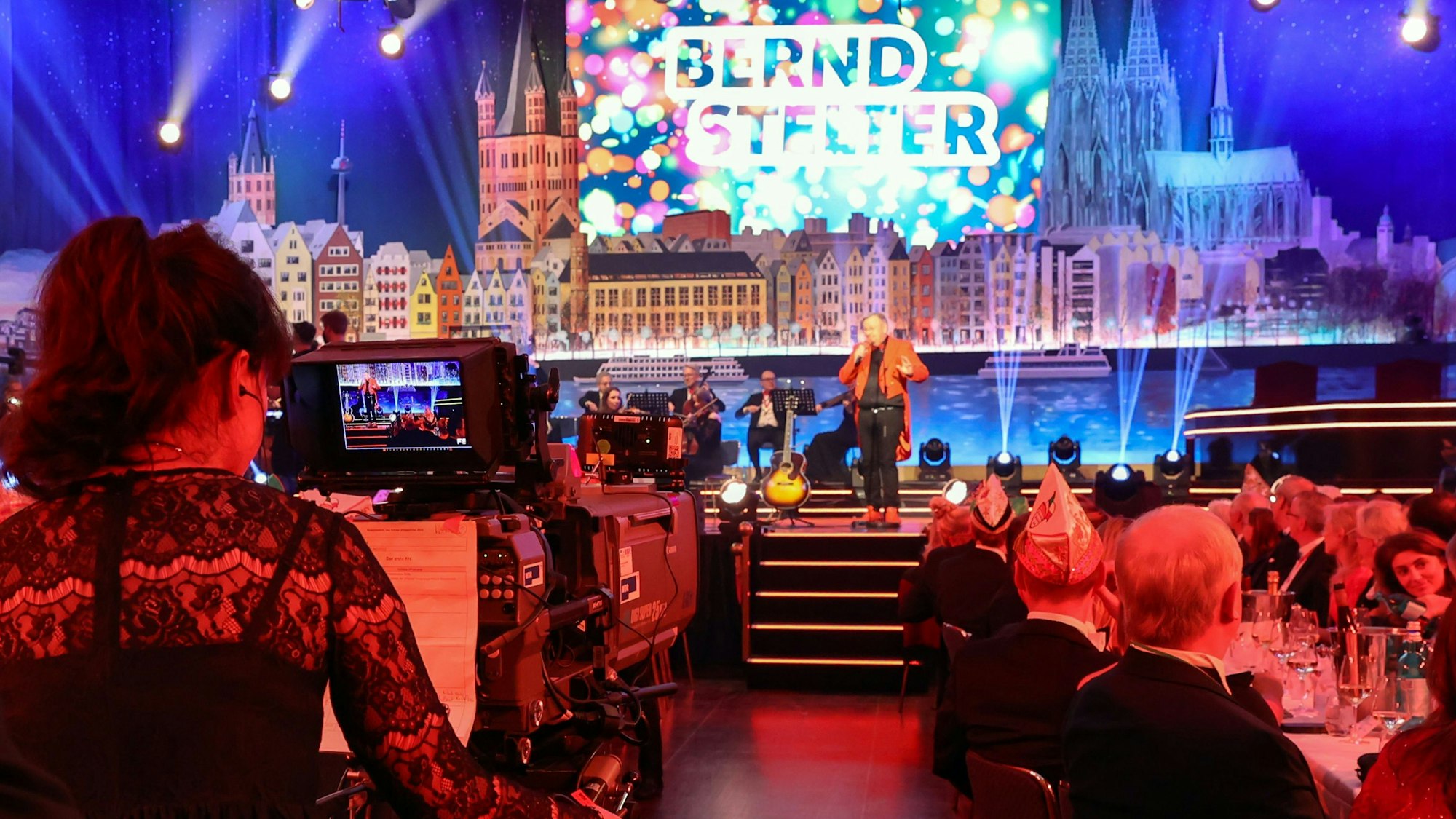 Eine Kamerafrau filmt aus der Saalmitte in Richtung Bühne, auf der Bernd Stelter steht.
