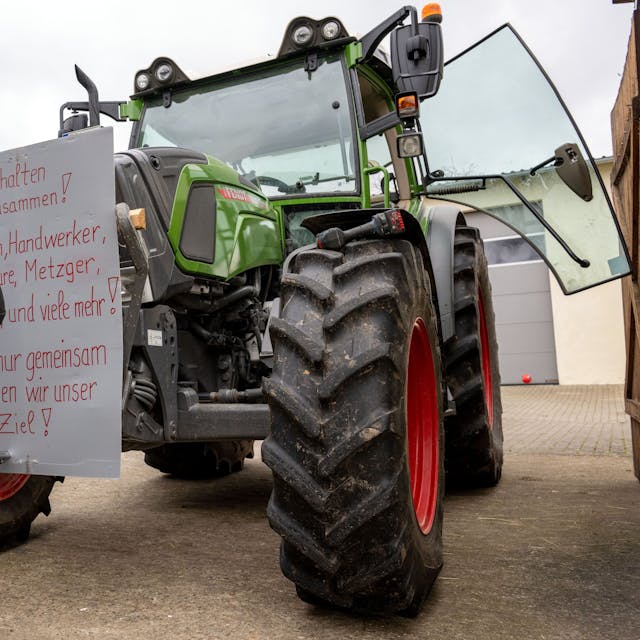 07.01.2024, Bayern, Wüstenwelsberg: Ein Mann befestigt ein Protestschild mit der Aufschrift «Wir alle halten zusammen! Bauern, Handwerker, Spediteure, Metzger, Bäcker, und viele mehr! Denn nur gemeinsam erreichen wir unser Ziel!» an einem Schlepper. Die Landwirte bereiten sich auf die anstehende Aktionswoche vor. Foto: Pia Bayer/dpa +++ dpa-Bildfunk +++