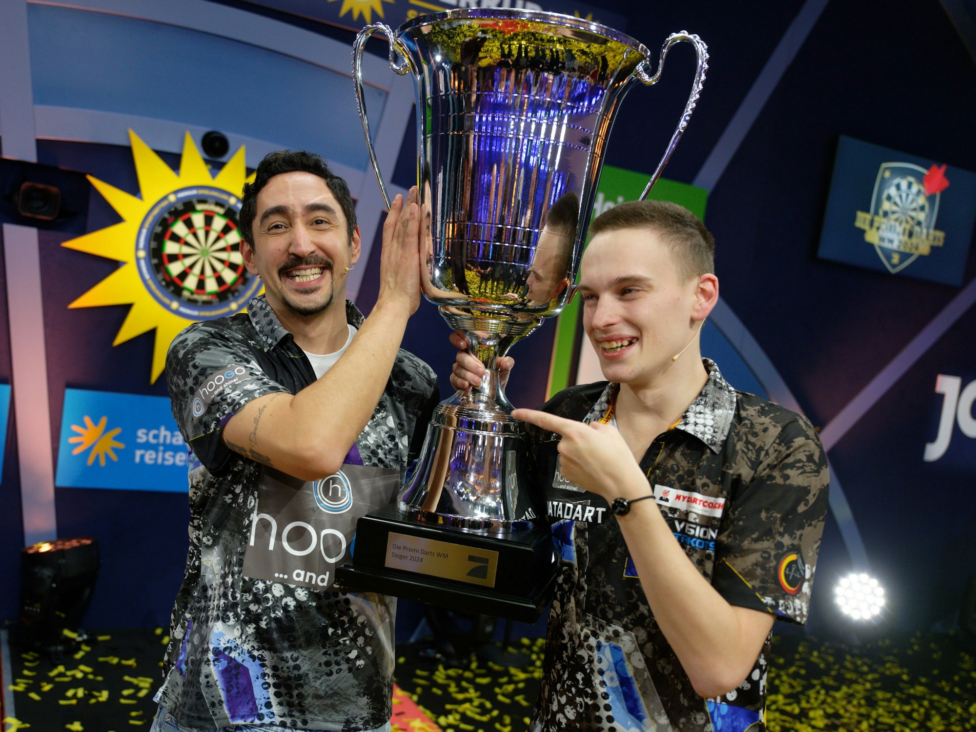 Die Gewinner der ProSieben Fernsehshow „Promi-Darts-WM 2024“: Eko Fresh (links) und Ricardo Pietreczko stehen mit ihrem Pokal auf der Bühne.