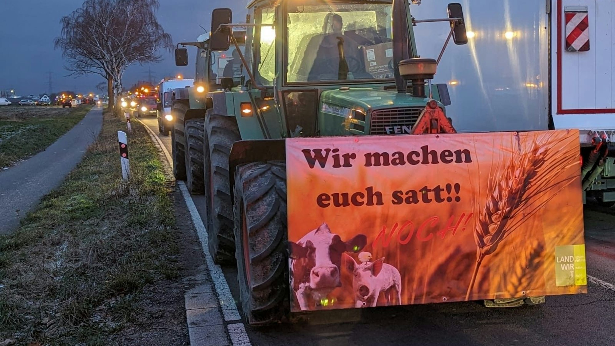 Auf dem Foto ist ein Traktor zu sehen. Auf einem Transparent steht „Wir machen euch satt!!“.