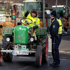 Das Bild zeigt einen Landwirt, der auf einem alten Traktor sitzt und mit einem Polizisten spricht.