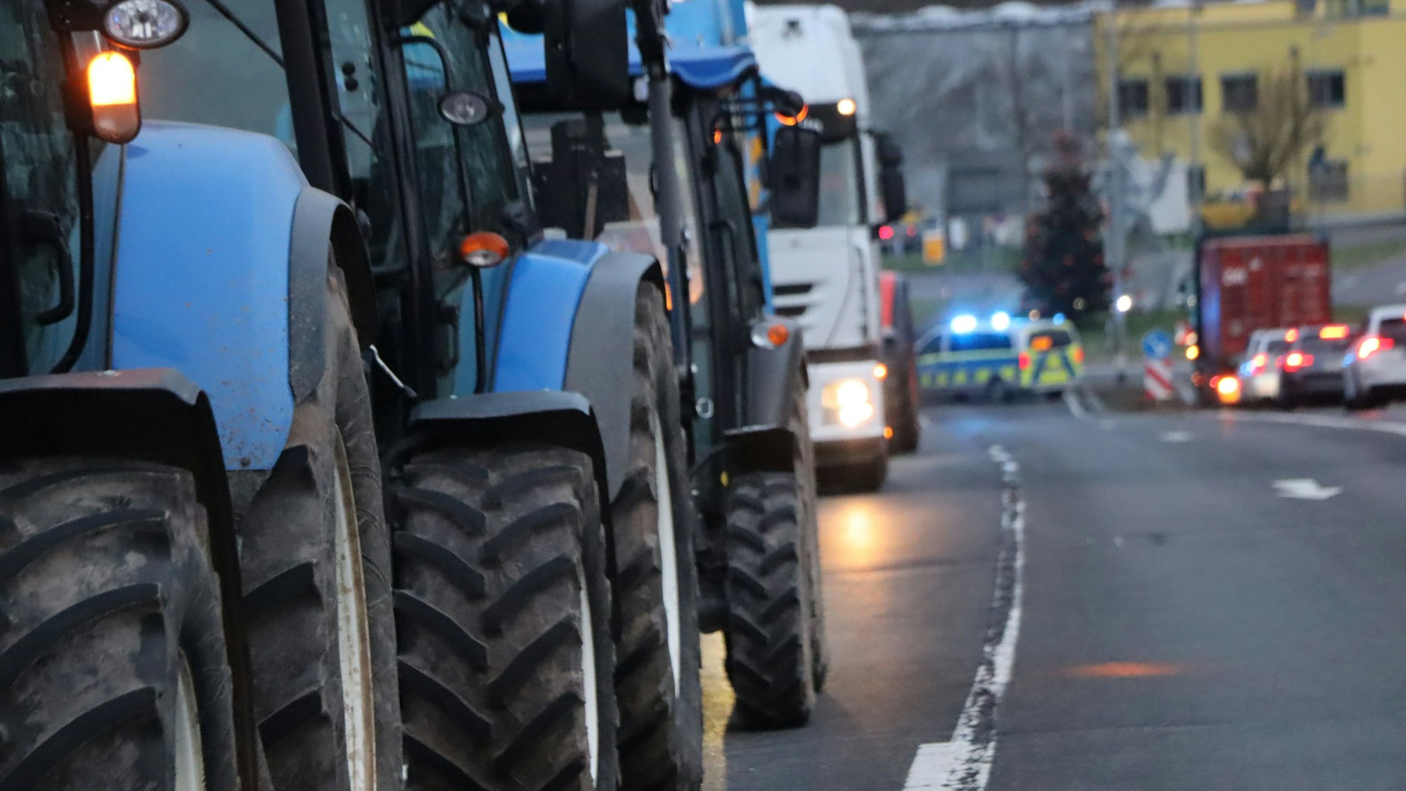 Auf dem Foto sind Traktoren zu sehen, dahinter Lkw und ein Polizeiwagen mit Blaulicht.