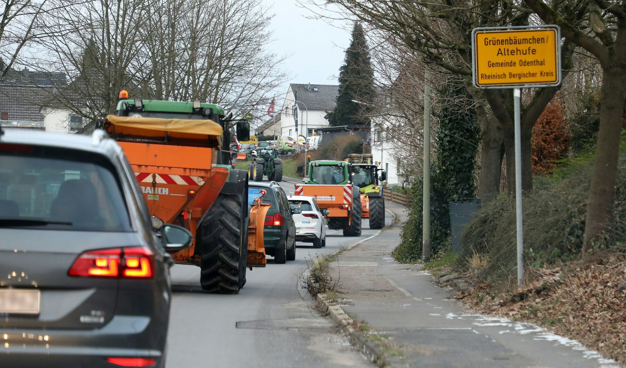 Am Ortsschild von Grünenbäumchen/Altehufe in der Gemeinde Odenthal ist eine Kolonne von Traktoren und Pkw zu sehen, die auf der B 506 in Richtung Bergisch Gladbach fahren.