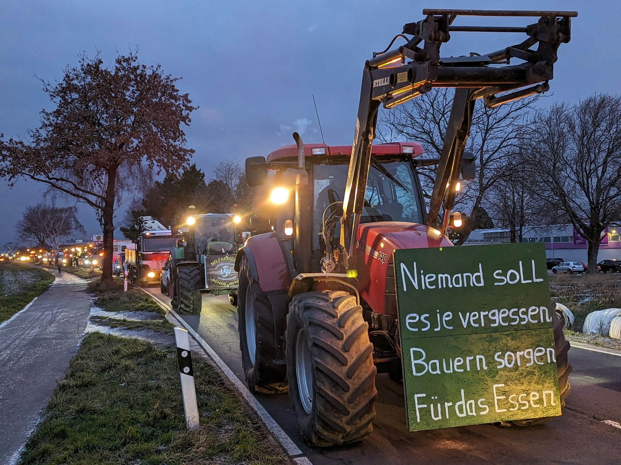 Ein Trecker mit dem Schild: „Niemand soll es je vergessen – Bauern sorgen für das Essen“. Dahinter eine Kolonne mit weiteren Fahrzeugen.