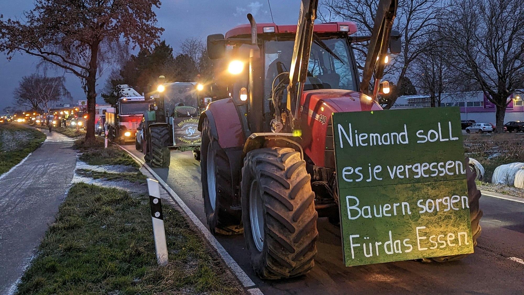 Auf dem Foto ist ein Traktor zu sehen. An seinem Kühler ist ein Schild angebracht: „Niemand soll es je vergessen: Bauern sorgen für das Essen“ ist darauf zu lesen.