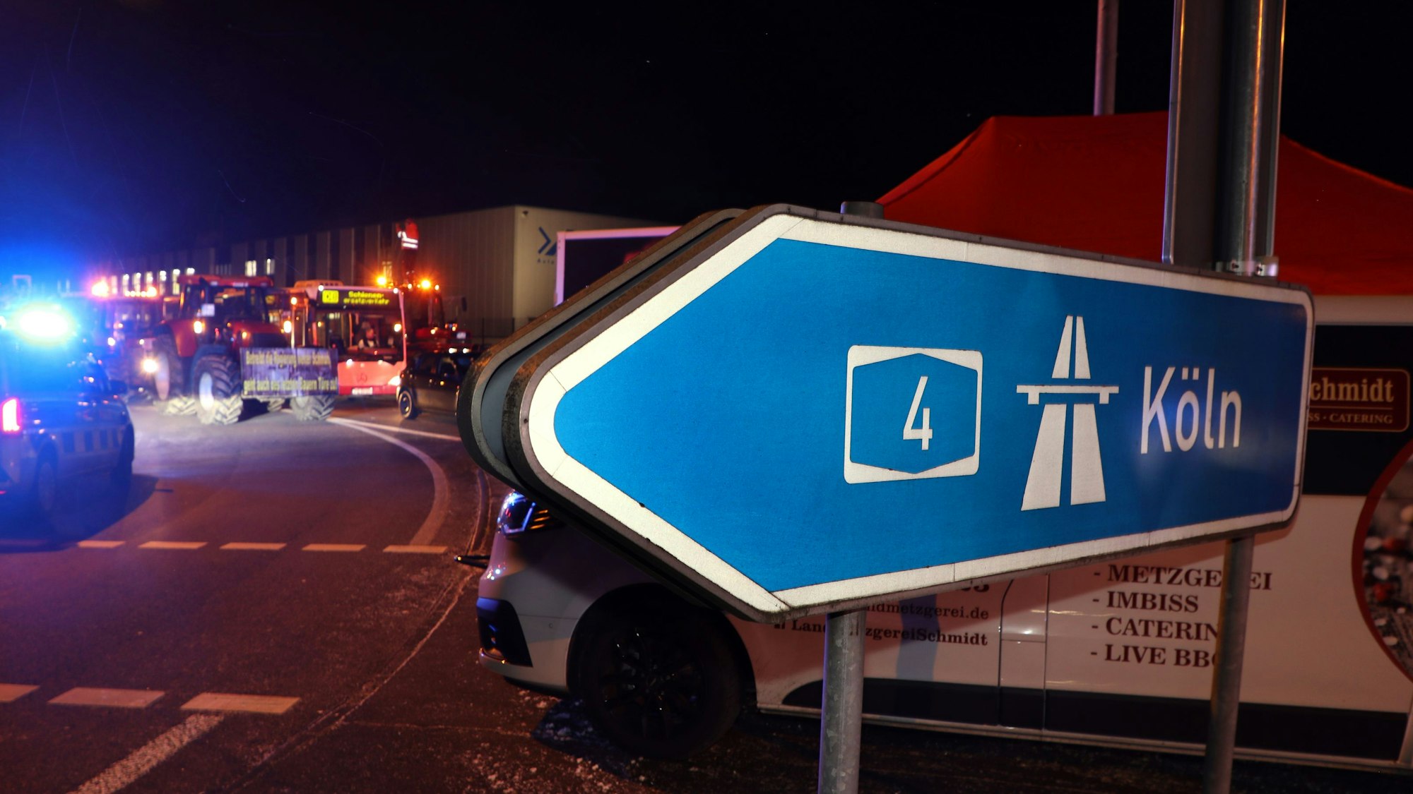 Hinter einem Autobahnhinweisschild mit der Aufschrift „Köln“ blockieren Traktoren die Abbiegespur zur Autobahn in Overath.