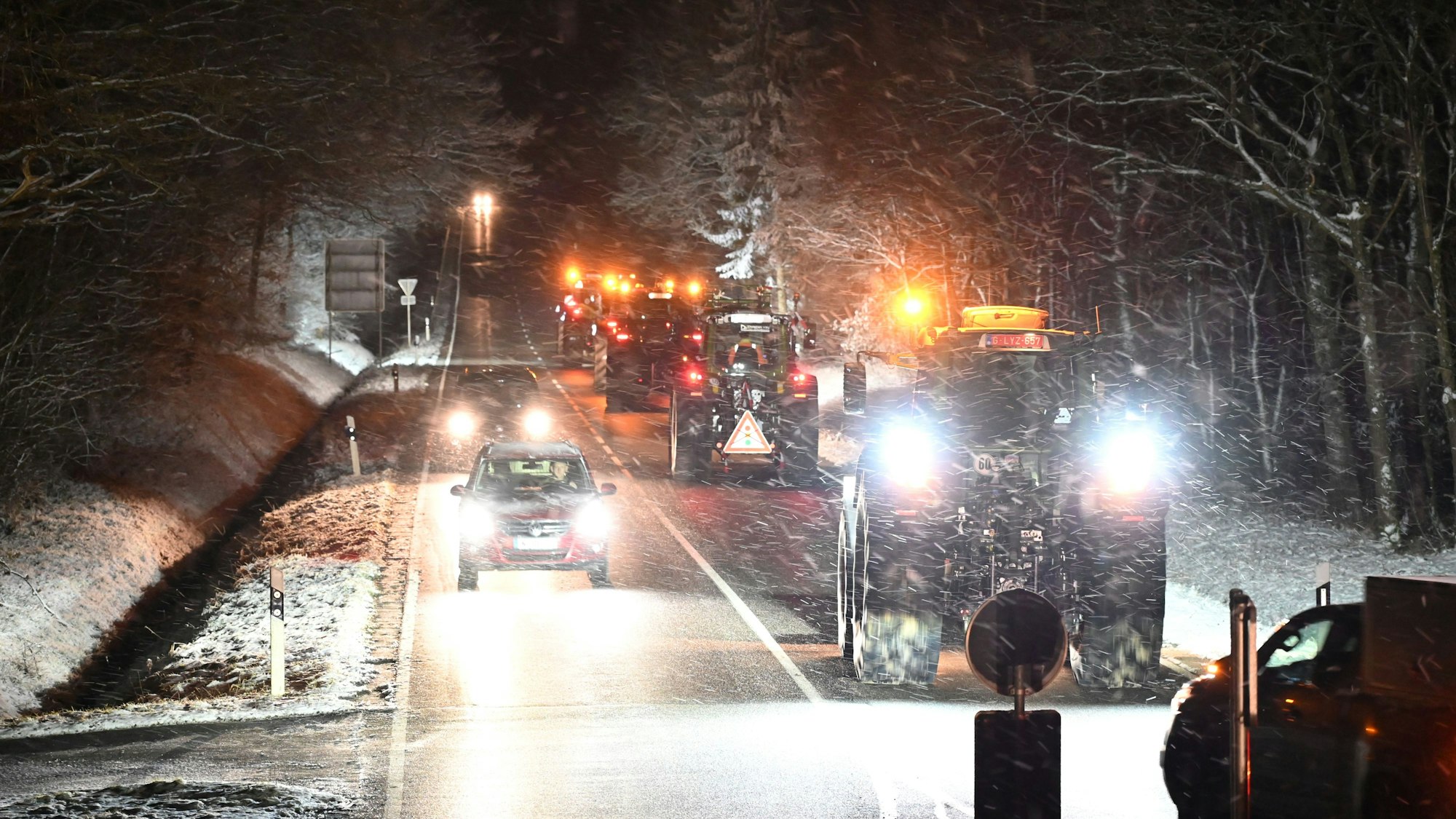 Schnee auf den Straßen, während die Traktoren im Licht der Schweinwerfer fahren.