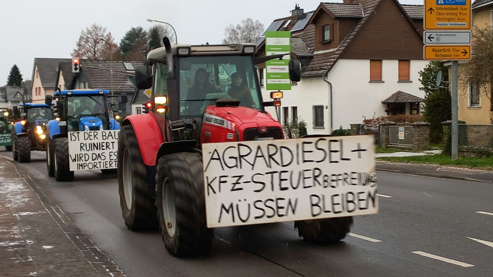 Mehrere Traktoren mit Protestschildern fahren eine Straße entlang.
