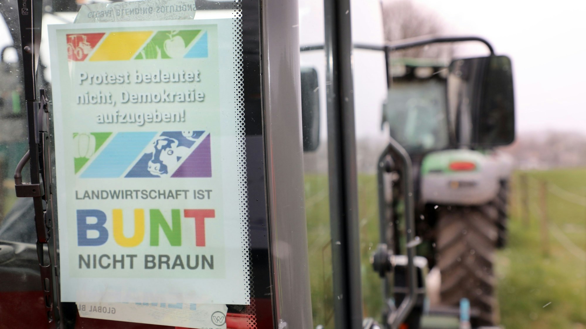 Ein Protestplakat mit der Aufschrift „Landwirtschaft ist bunt nicht braun“ klebt an einer Traktorscheibe.