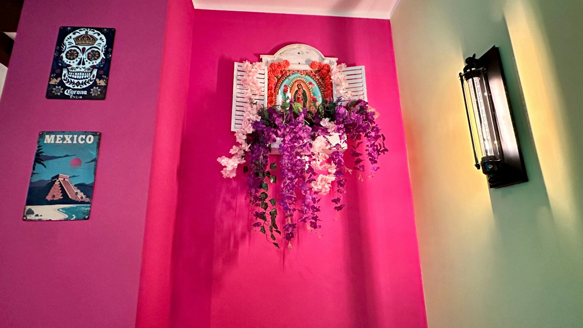 An einer pink gestrichenen Wand hängen Bilder und Wandschmuck aus Mexiko.