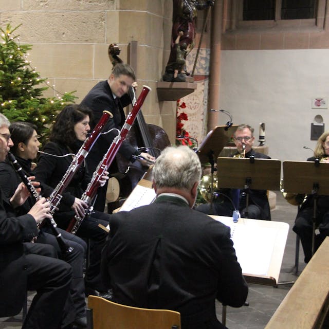 Sieben Musikerinnen und Musiker, unter anderem mit Klarinette, Fagott und Kontrabass, spielen in der Martinskirche. Vom Bassisten abgesehen, sitzen sie. Im Hintergrund stehen die Weihnachtskrippe und ein Weihnachtsbaum.&nbsp;