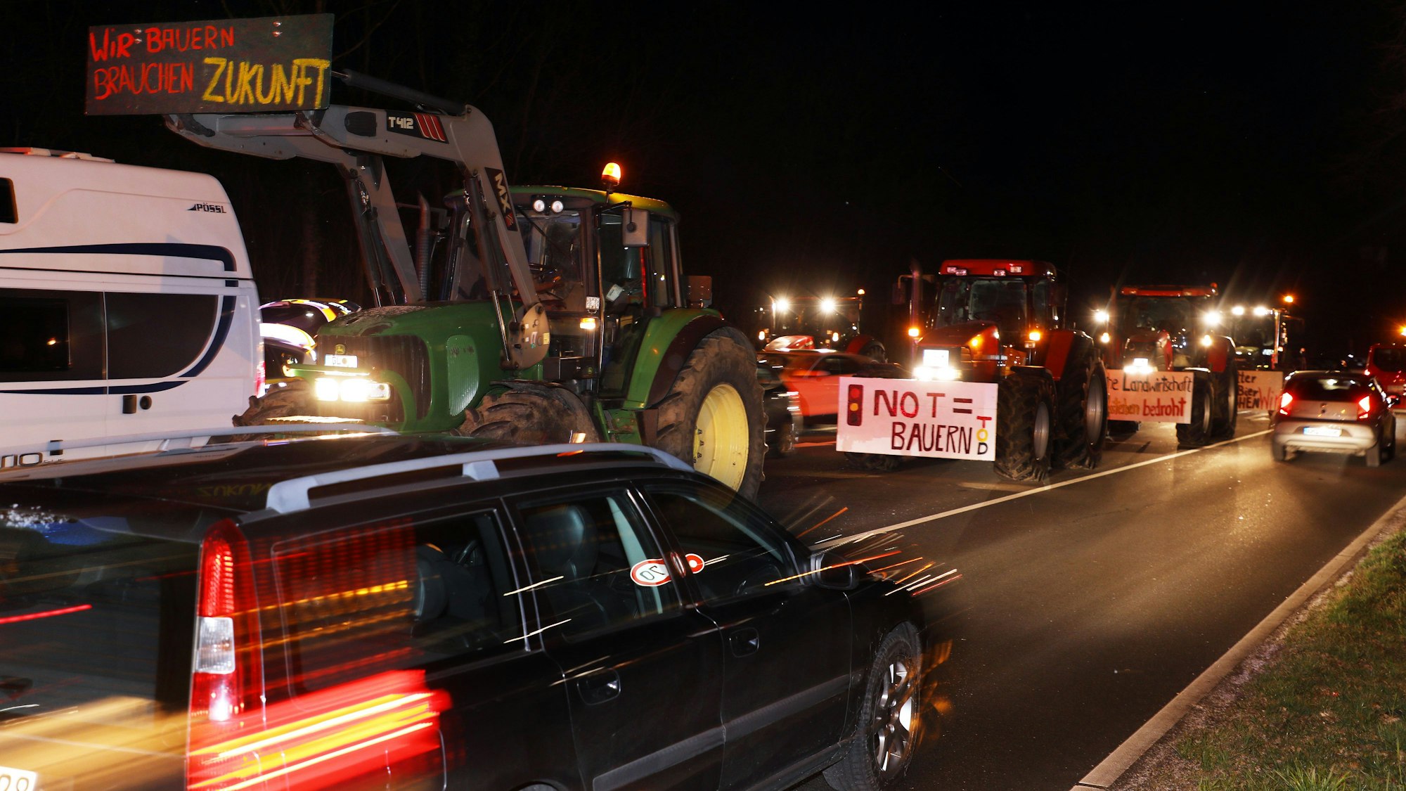 Traktoren mit Protestplakaten stehen auf einer nächtlichen Straße.