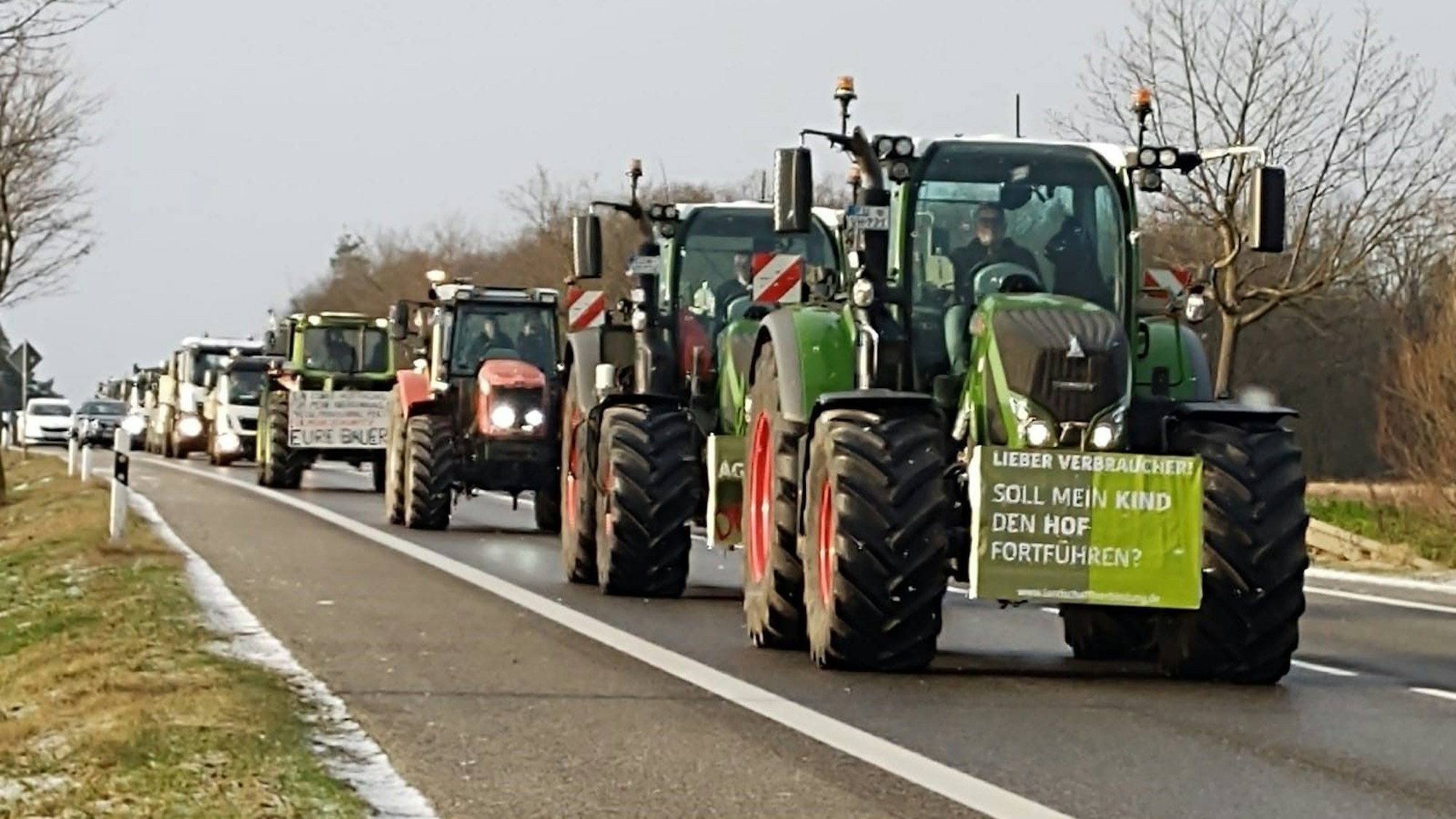Traktoren mit Protestplakaten fahren auf der B266, dahinter ist eine Autokolonne.