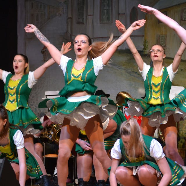 Tänzerinnen der Hovener Jungkarnevalisten zeigen auf der Bühne ihr Programm, die Arme in die Höhe gestreckt. Sie tragen grün-gelbe Kostüme.