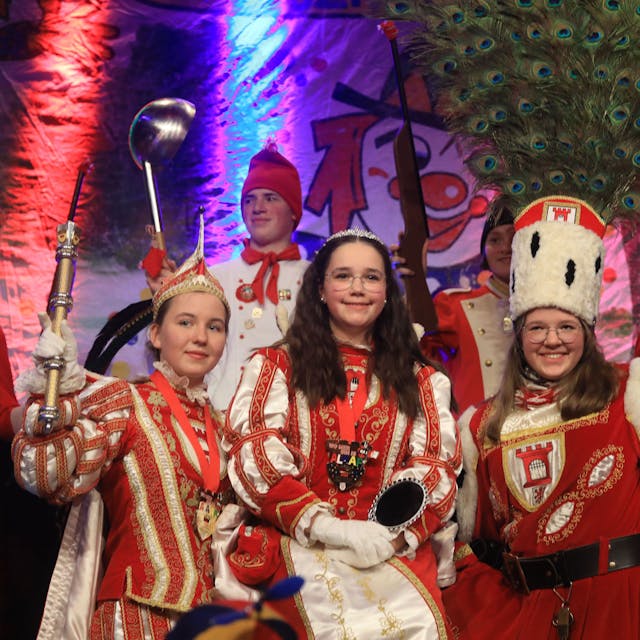 Prinz Ella I., Jungfrau Marie und Bauer Pia (v.l.) stehen in vollem Kinderdreigestirns-Ornat auf der Bühne.