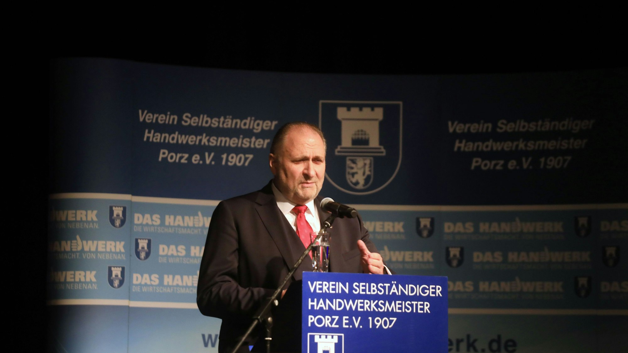 Ein Mann mit roter Krawatte steht an einem Rednerpult.