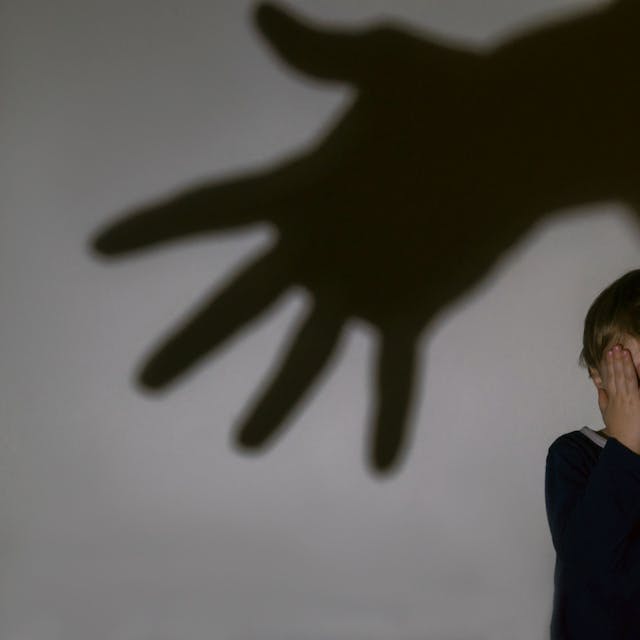 Ein kleiner Junge sitzt vor einer Wand und hält vor Schrecken seine Hände vors Gesicht. An der Wand ist ein großer Schatten einer ausgestreckten Hand zu sehen.&nbsp;