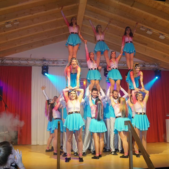 Die Tänzerinnen und Tänzer der Gruppe Bürvenicher Danzspektakel bilden auf der Bühne eine dreistöckige Menschenpyramide. Sie tragen blau-weiße Kostüme.&nbsp;