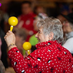 Das Bild zeigt eine Seniorin, die mit zwei Sambarasseln im jecken Rhythmus mitfeiert.