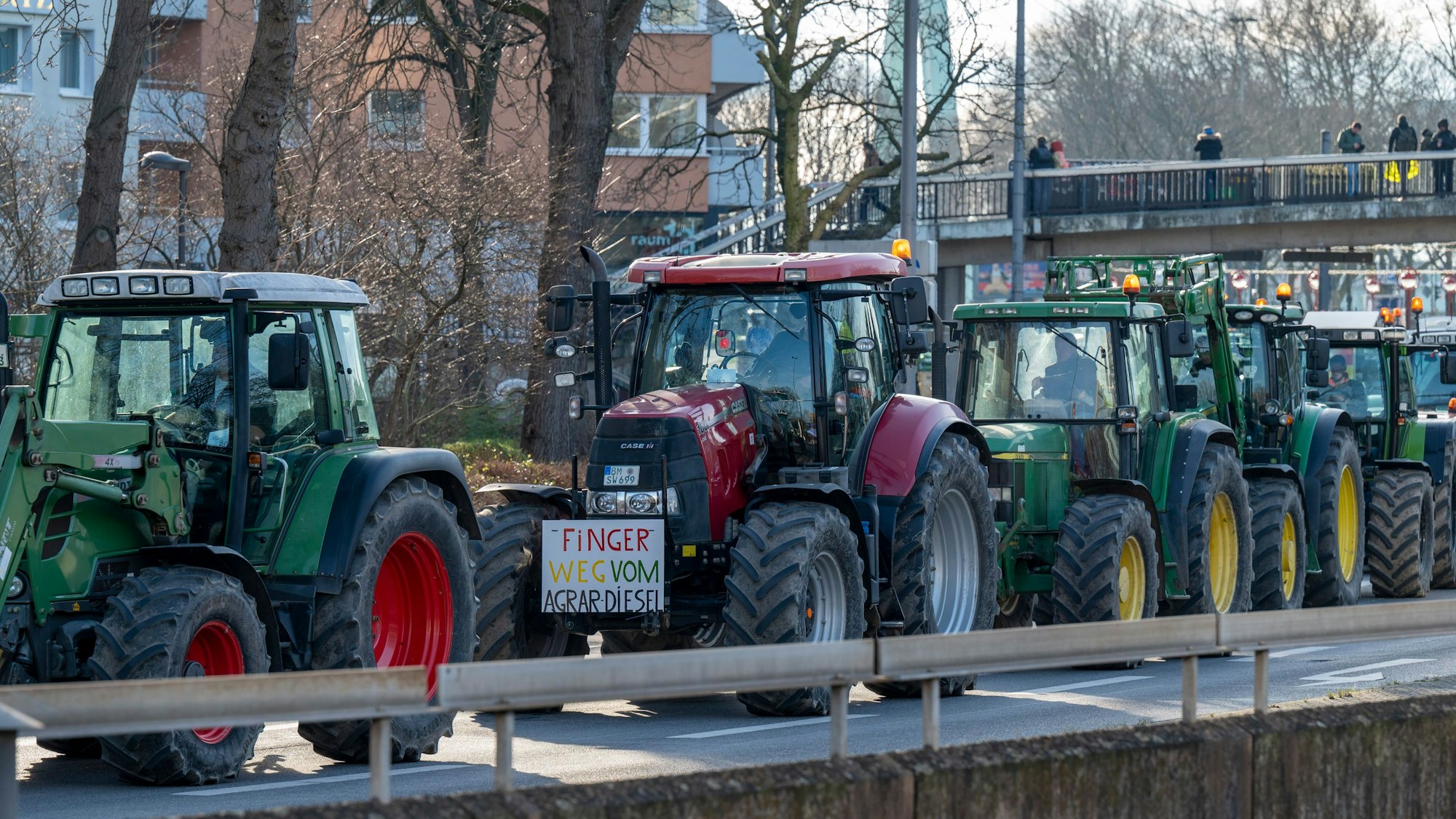 Ein Zug von fünf Traktoren fährt über die Opladener Straße in Deutz. Am zweiten Traktor ist ein Plakat mit der Aufschrift „Finger weg vom Agrardiesel“ angebracht. Im Bildhintergrund ist ein Stützpfeiler der Deutzer Brücke zu sehen.
