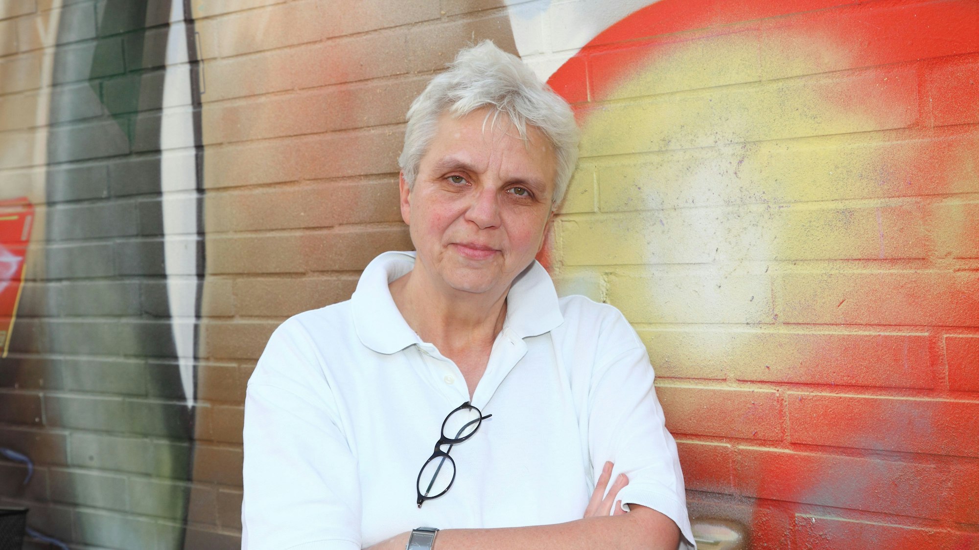 Brigitte Maser lehnt mit weißem Poloshirt an einer farblich dekorierten Hauswand.