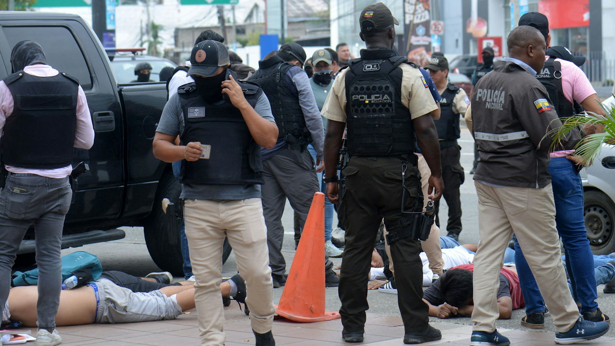 TOPSHOT - Ecuadorean police officers fuard the arrested suspects outside Ecuador's TC television channel after unidentified gunmen burst into the state-owned television studio live on air on January 9, 2024, in Guayaquil, Ecuador, a day after Ecuadorean President Daniel Noboa declared a state of emergency following the escape from prison of a dangerous narco boss. Gunshots rang out on live TV in violence-torn Ecuador as armed men carrying rifles and grenades stormed the studio shortly after gangsters vowed a "war" against the president's plans to reclaim control from "narcoterrorists". (Photo by STRINGER / AFP)